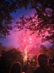 Red fireworks fountain shooting above Crystal Lake with silhouettes of several people in the foreground.
